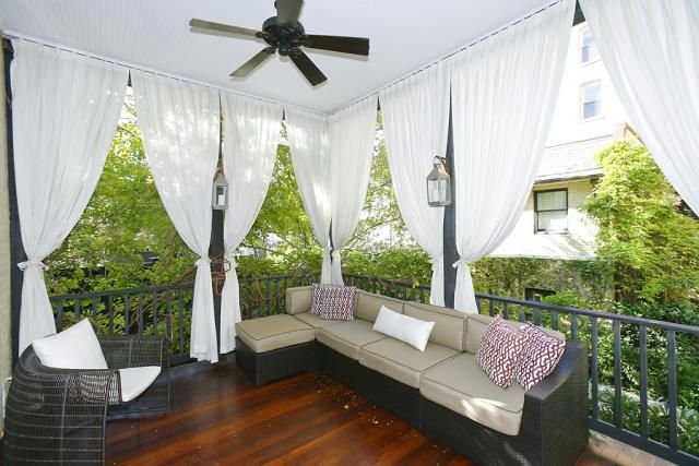 Backyard pergola with sheer green curtains and ceiling fan above lounge seating.