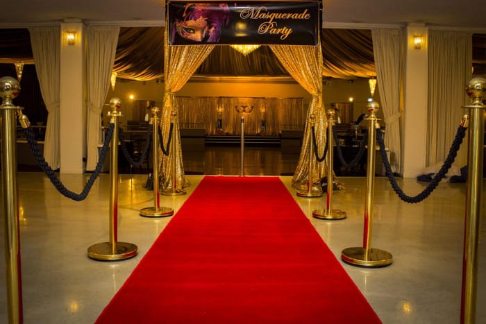Red carpet with gold stanchions and velvet ropes under purple lighting