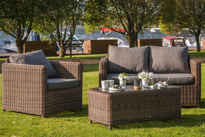 Dark wicker outdoor sofa with armchairs and cushions placed on grass