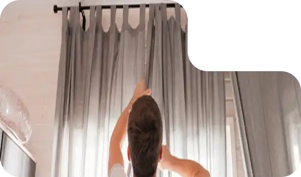 Man installing or adjusting grey curtains on a curtain rod in a modern room