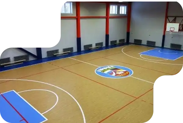 Indoor basketball court with tan flooring, blue key areas, and a colorful custom center-court logo.