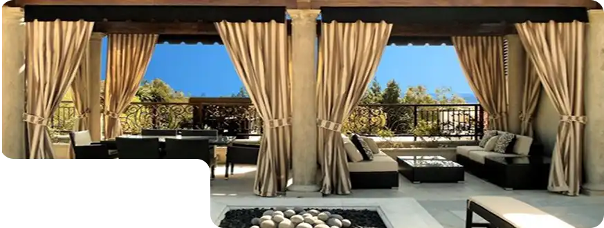 Luxurious patio with beige all-weather outdoor curtains tied to columns, surrounding lounge furniture under clear blue skies.