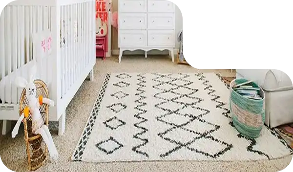 White nursery rug with black geometric diamond pattern placed beside crib and basket.