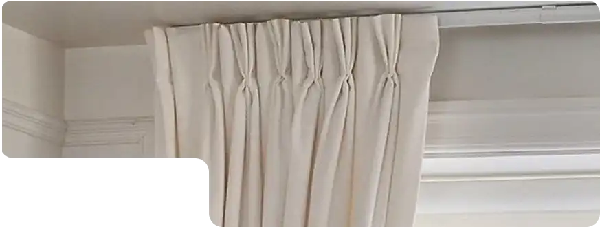 Close-up view of cream pinch pleat curtains mounted on a ceiling track.