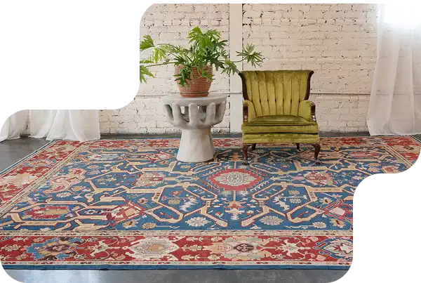 Traditional Persian rug with red and blue geometric patterns styled in a modern living room with a green chair and potted plant.