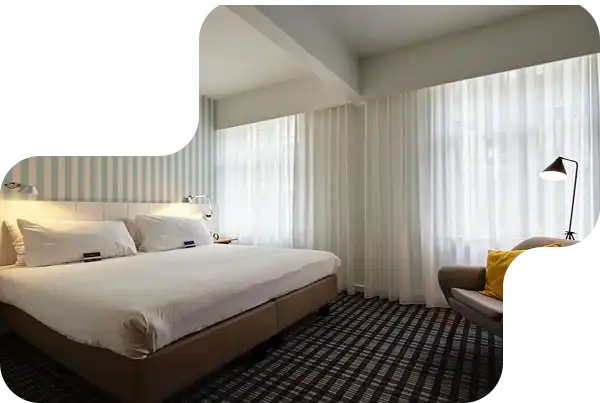 Contemporary hotel bedroom with large bed, sheer white curtains, and checkered carpet flooring