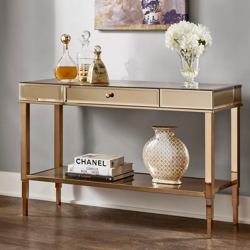 Gold and glass console table with two drawers and lower shelf, decorated with vase and books.