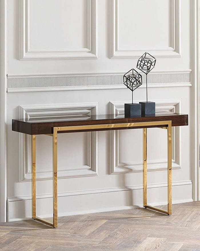 Slim rectangular console table with black top and gold frame, placed against a white wall.