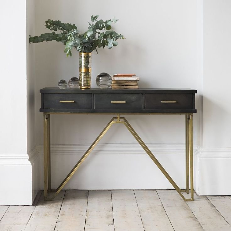 Black console table with brass base and two drawers, minimalist decor with a vase.