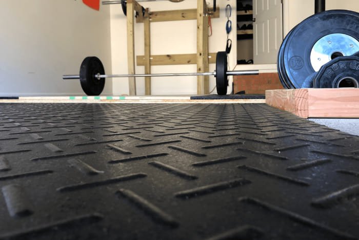 Close-up view of diamond plate patterned gym mats used under weightlifting equipment.