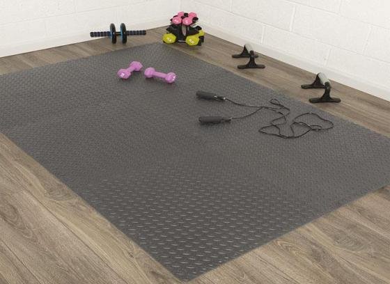 Home workout setup with interlocking foam gym mats, dumbbells, and resistance gear.